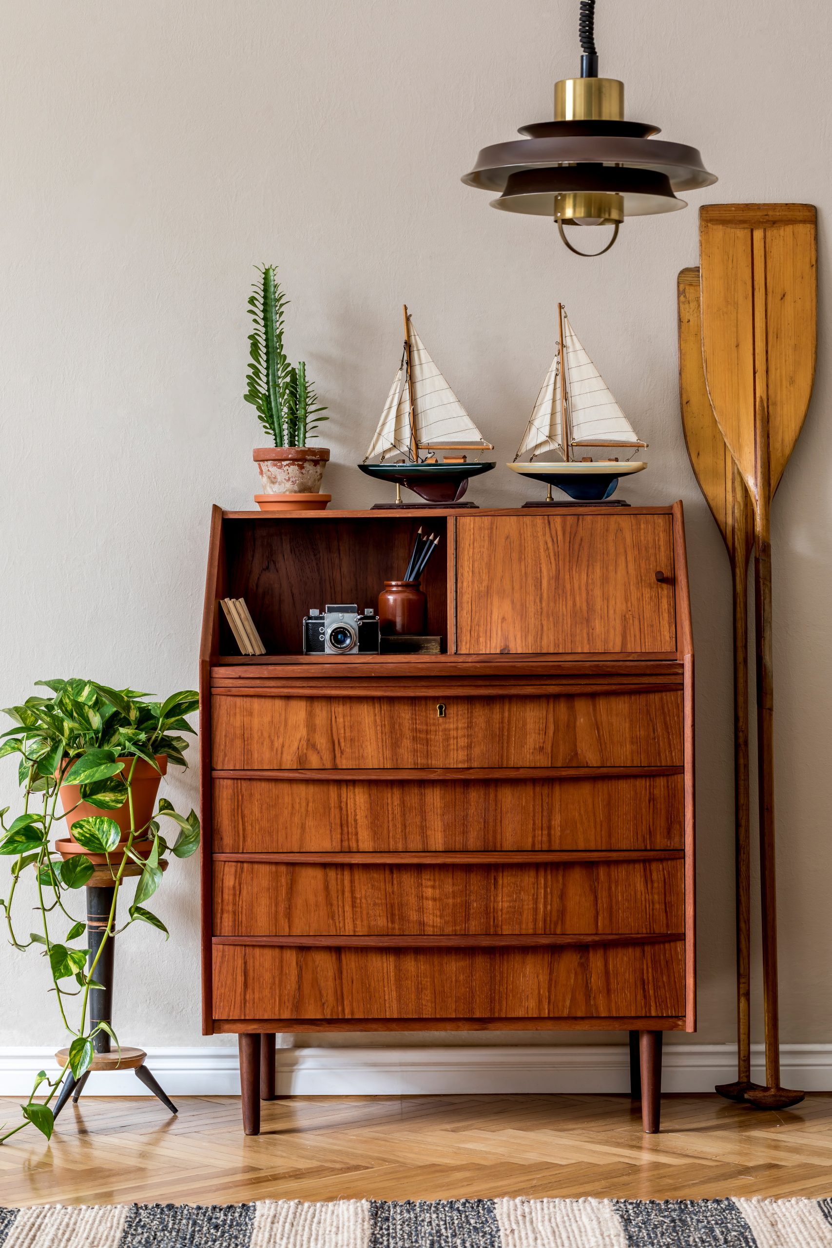 Stylish and vintage interior design of living room with wooden retro commode, plants, ships, paddle, map and elegant personal accessories. Mock up poster frame on the wall. Template. Home decor.