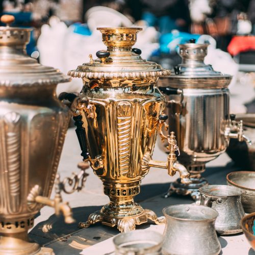 Shiny Bright Samovars Stand In A Row. Tea Party Concept And Hospitality. Traditional Russian Samovar At Flea Market. Vintage Copper Samovar. Since Ancient Times In Russia, All Guests Were Offered To Drink Tea From A Samovar. Most Famous Were Tula Samovars. Samovars Were Made Of Various Metals, Decorated With Various Ornaments.